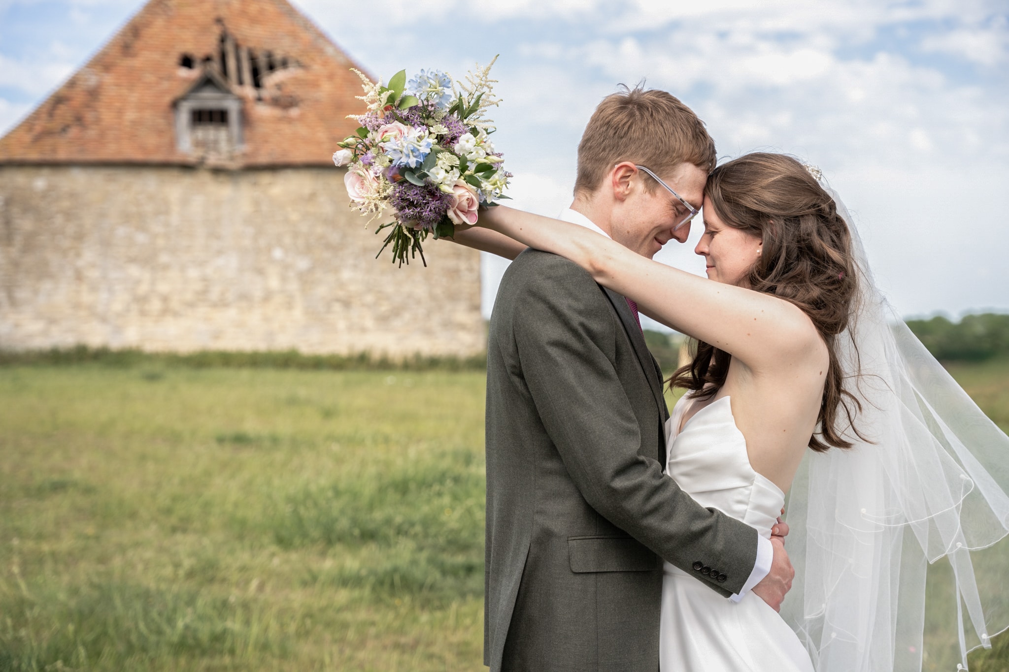 Bride and groom forehead to forehead with bouquet at Notley Tythe Barn