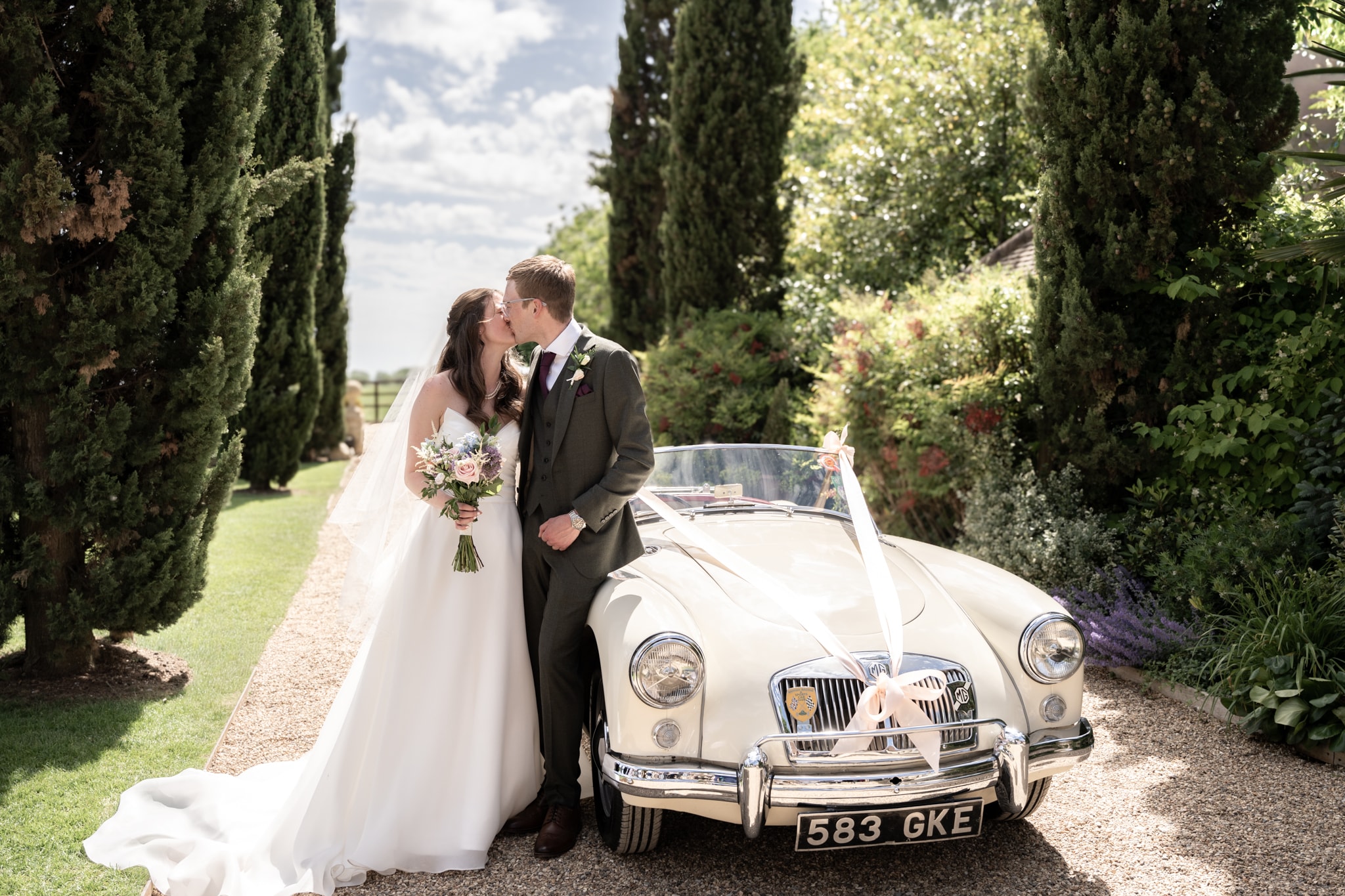 Bride and groom kissing beside vintage MG wedding car at Notley Tythe Barn