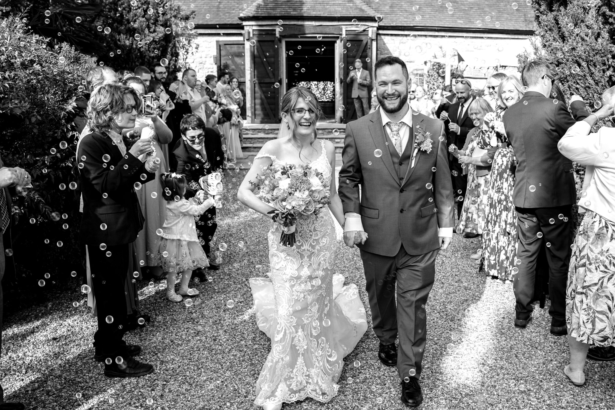 Black and white — bride and groom walking through bubble exit at Notley Tythe Barn