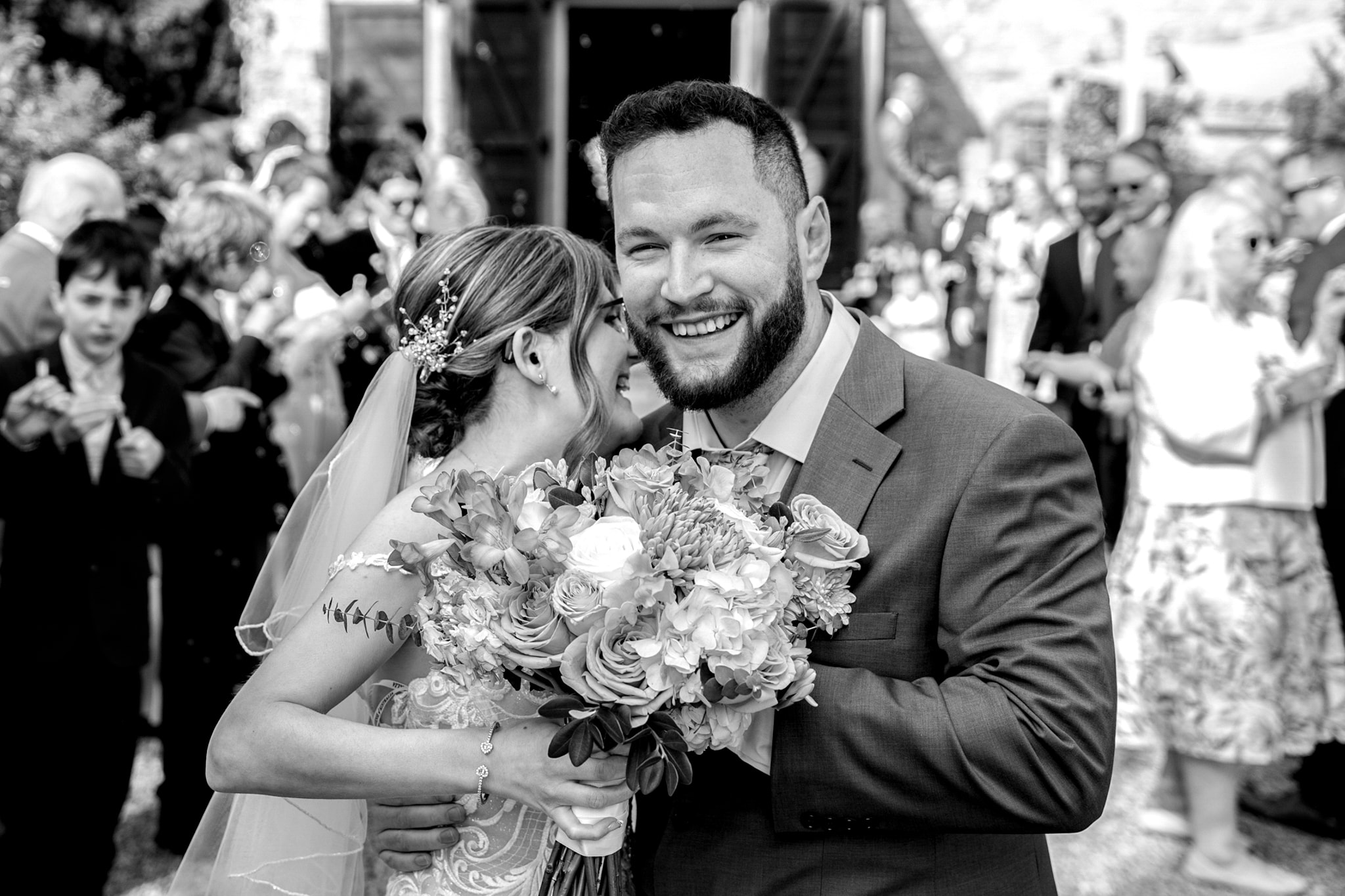 Black and white — bride and groom smiling together with bouquet at Notley Tythe Barn