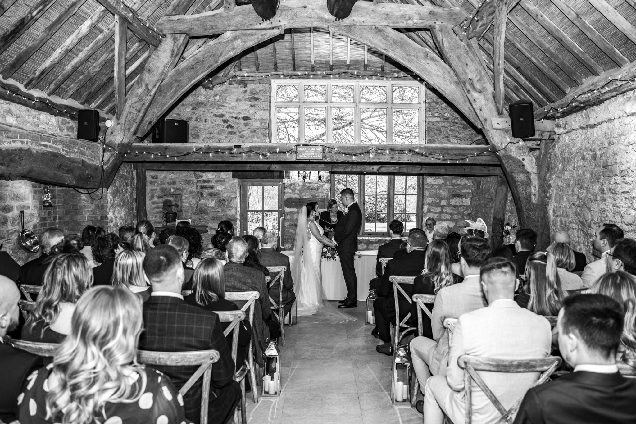 Wedding ceremony inside Notley Tythe Barn stone barn with fairy lights and full congregation
