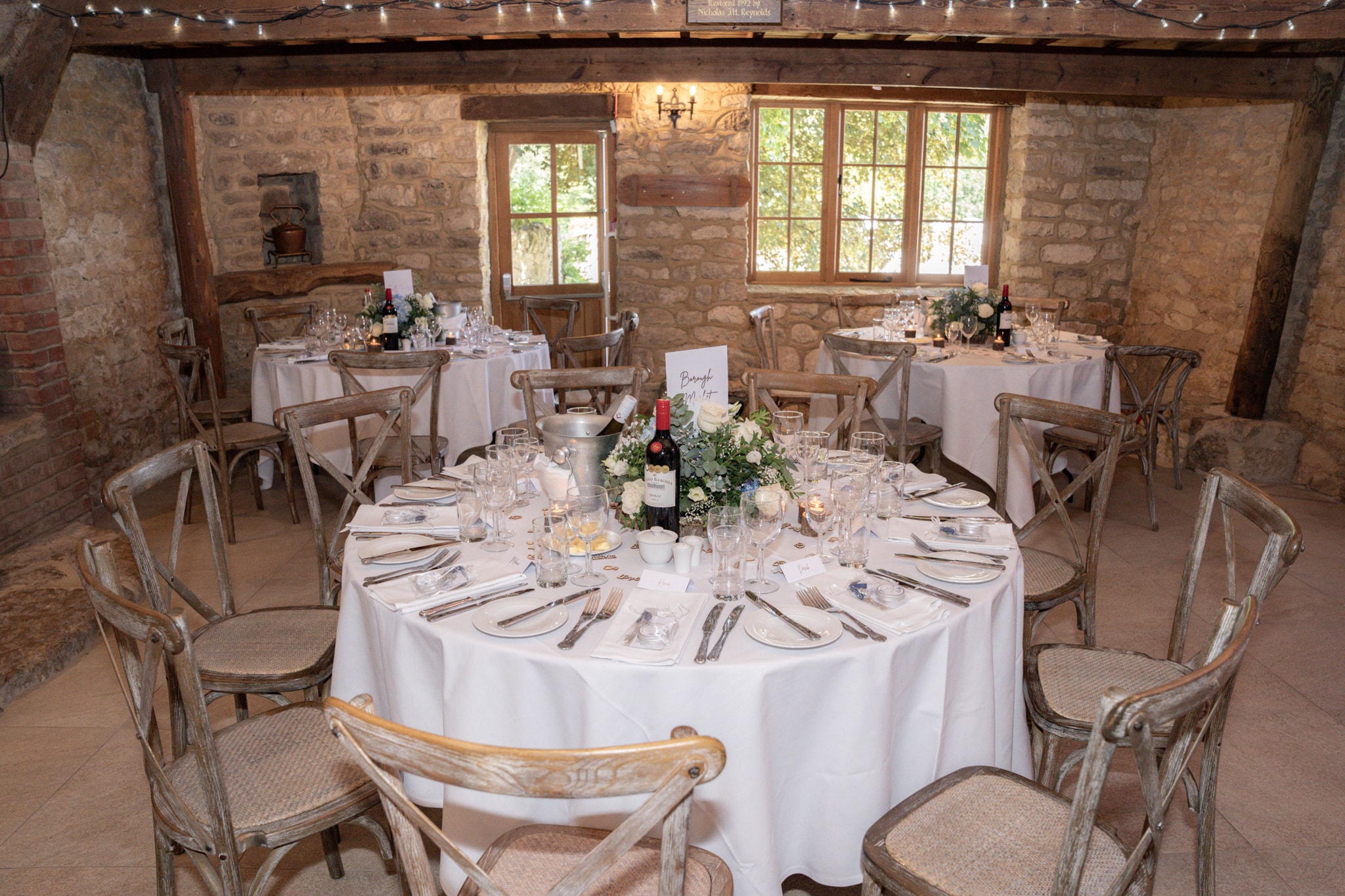 Elegant wedding reception room inside Notley Tythe Barn with stone walls, fairy lights and dressed round tables