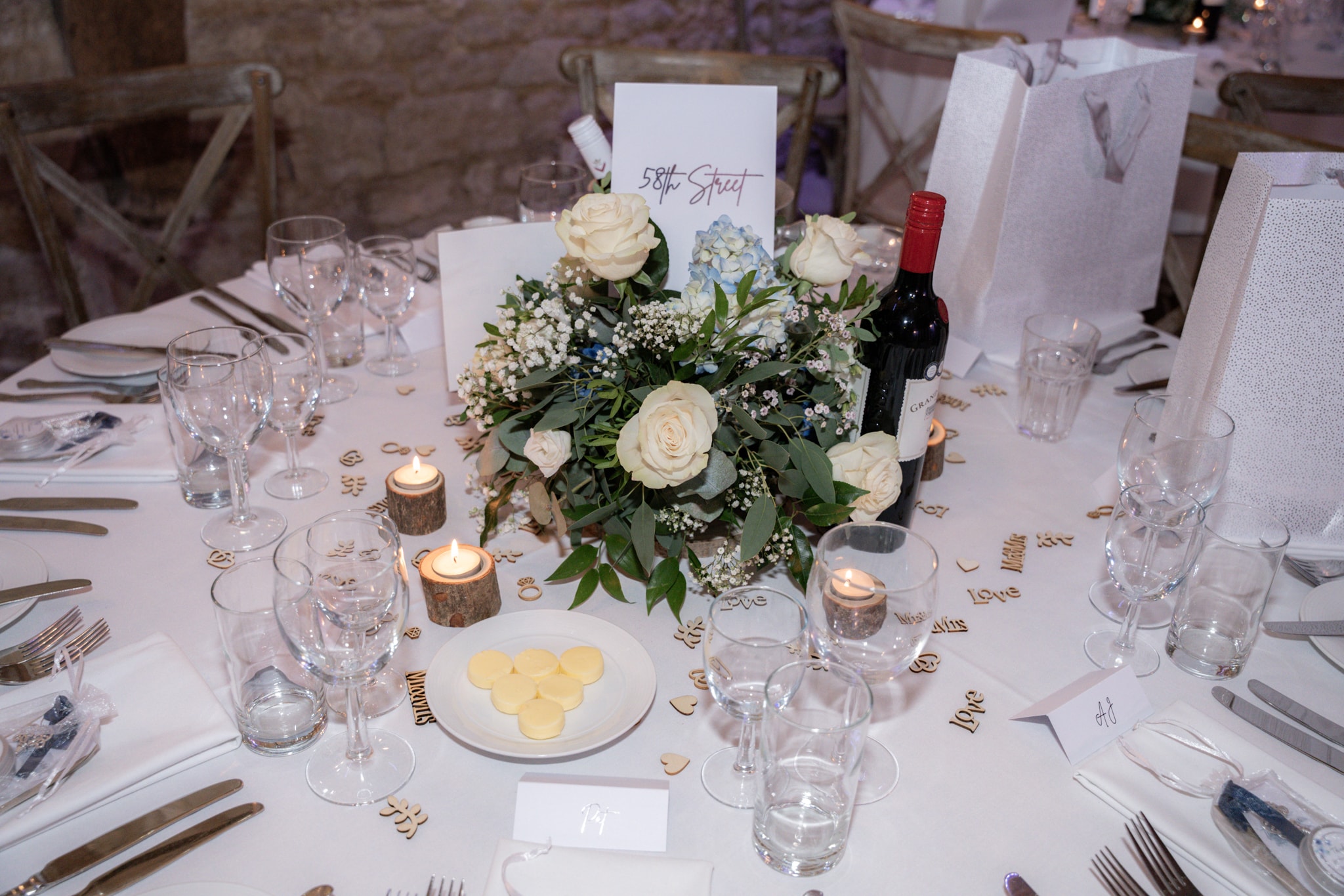 Close-up of wedding reception table centrepiece with white roses, candles and wooden confetti at Notley Tythe Barn