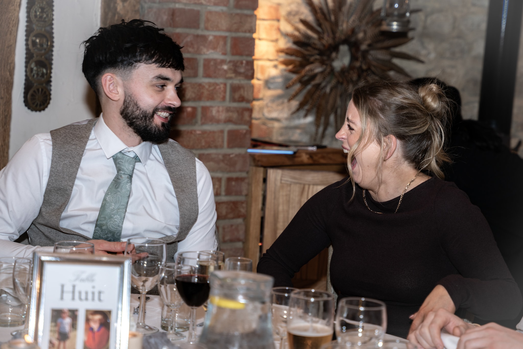 Wedding guests laughing together at dinner table inside rustic Notley Tythe Barn reception