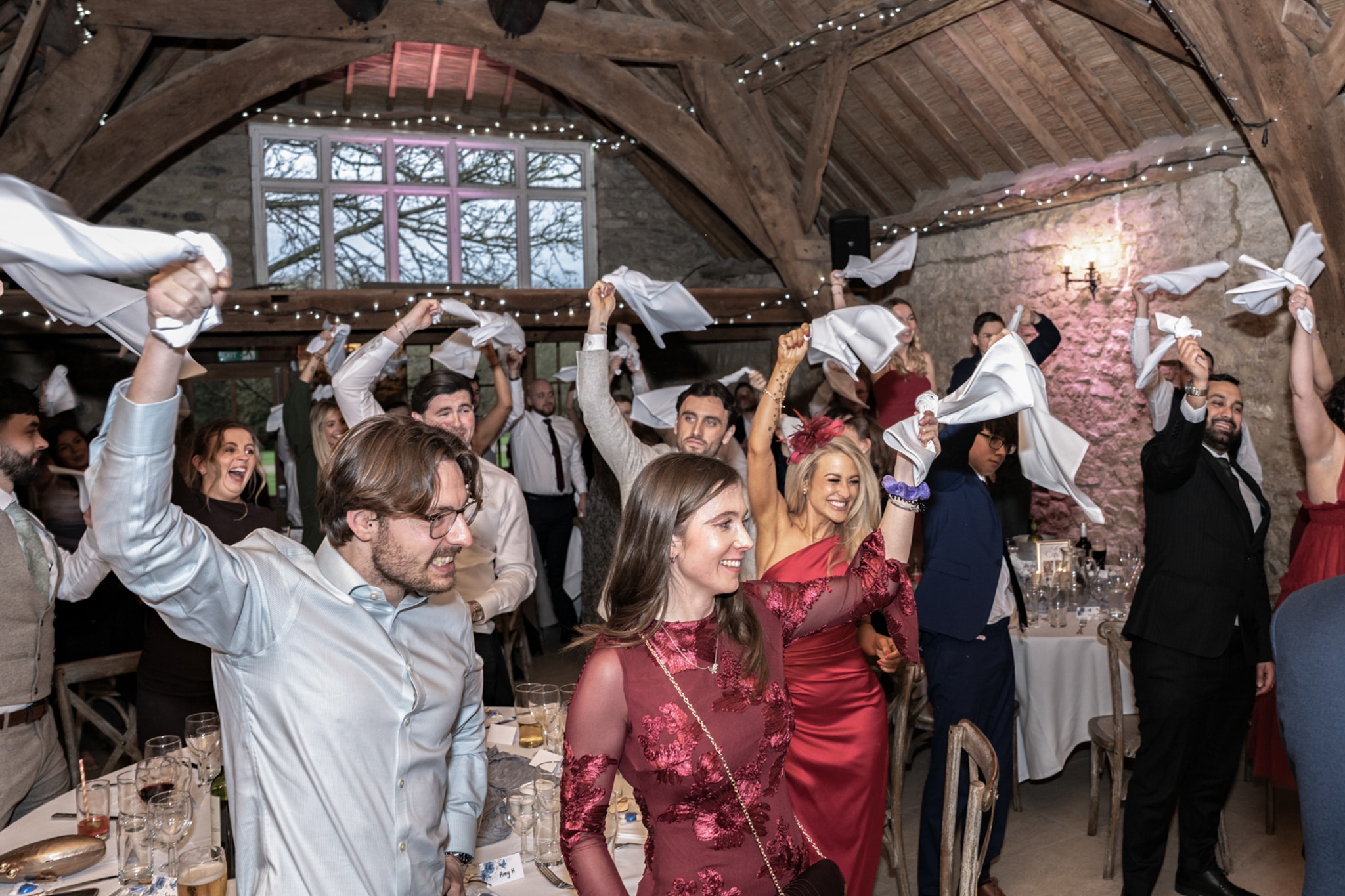 Wedding guests waving napkins in joyful celebration as couple enter the reception at Notley Tythe Barn