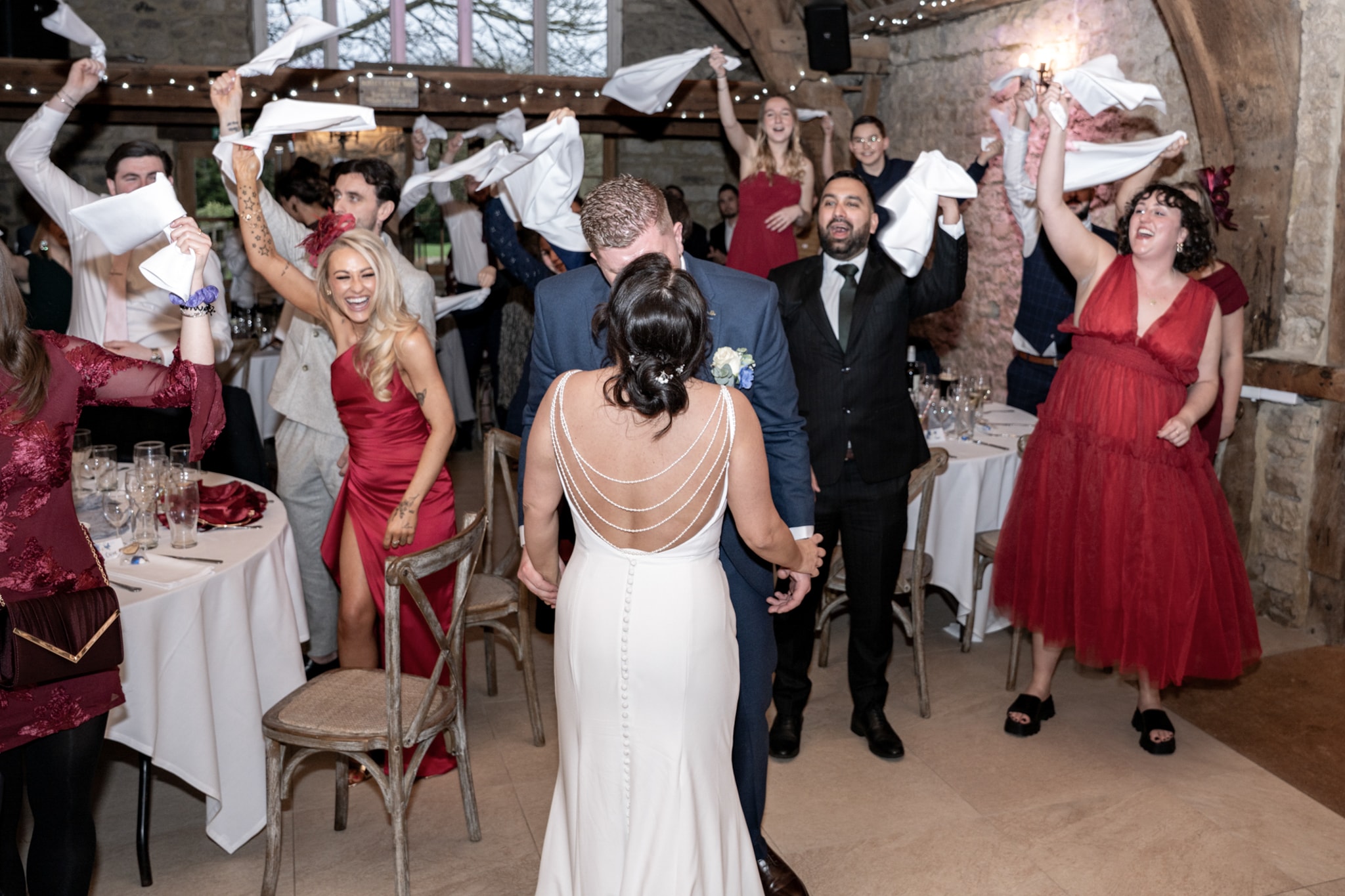 Bride and groom kissing as guests wave napkins in celebration inside Notley Tythe Barn reception