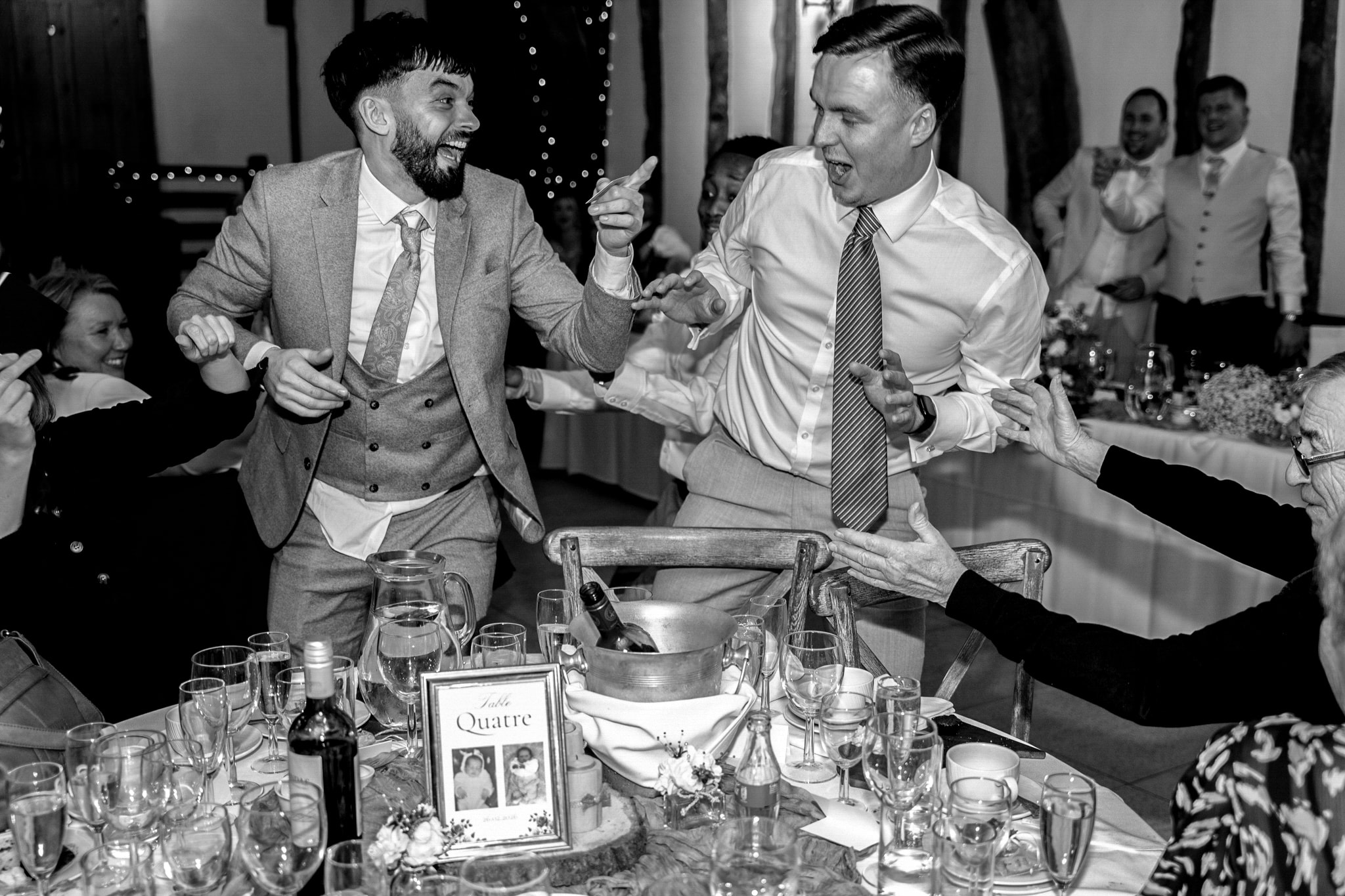 Black and white photo of two groomsmen dancing and celebrating at wedding reception inside Notley Tythe Barn