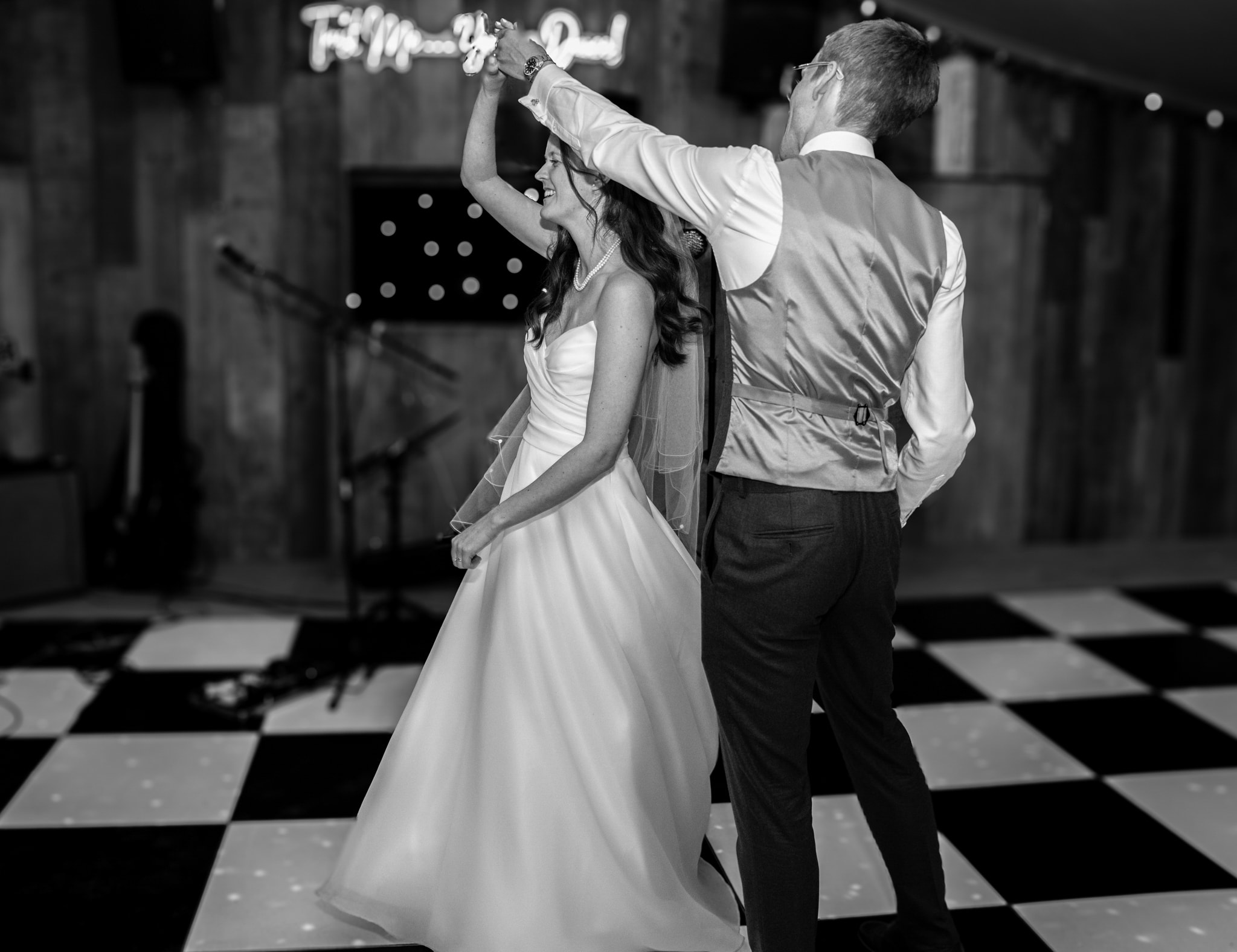 Bride and groom first dance black and white on checkered dance floor at Notley Tythe Barn with neon sign behind