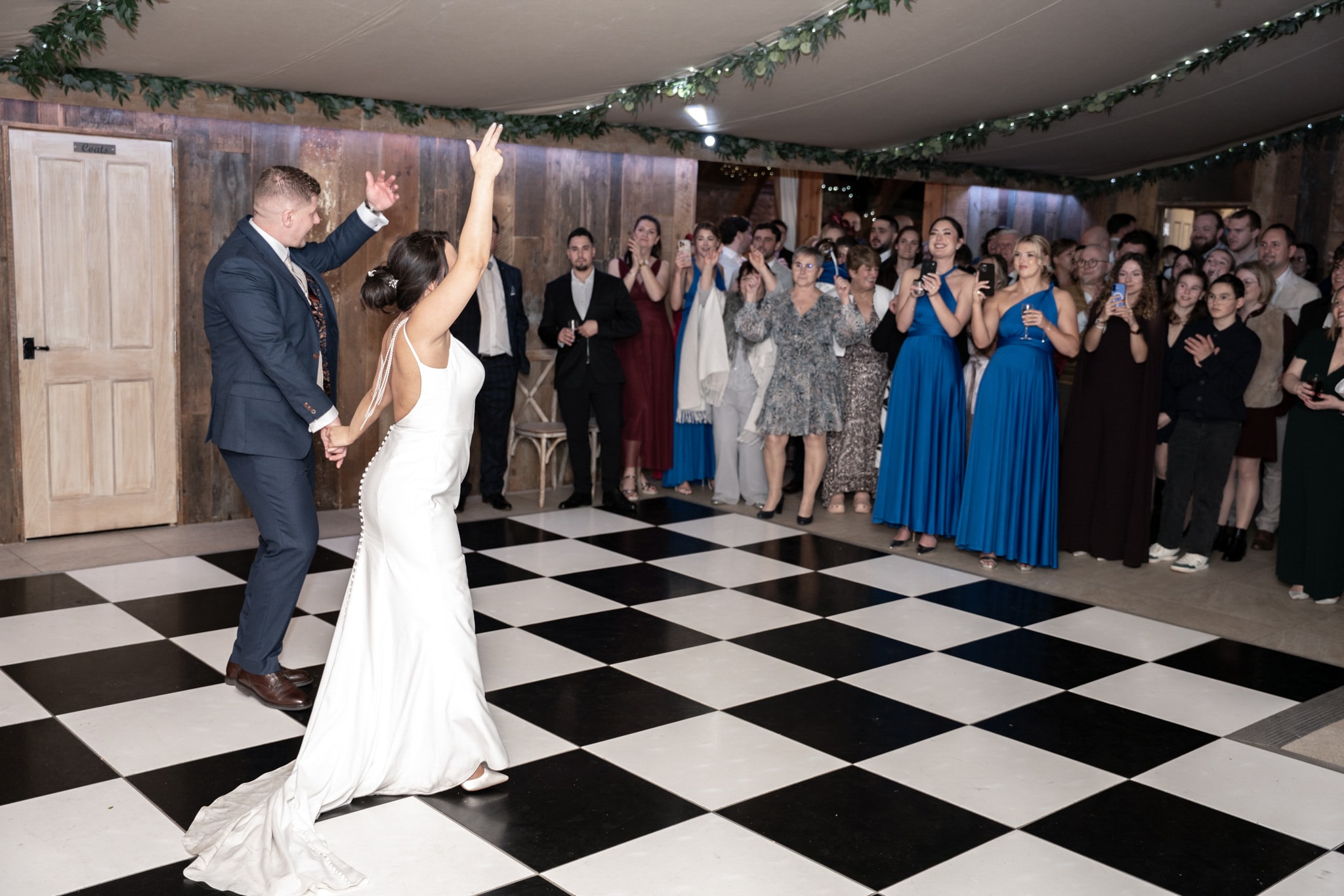 Bride and groom first dance in colour on checkered floor with guests watching at Notley Tythe Barn