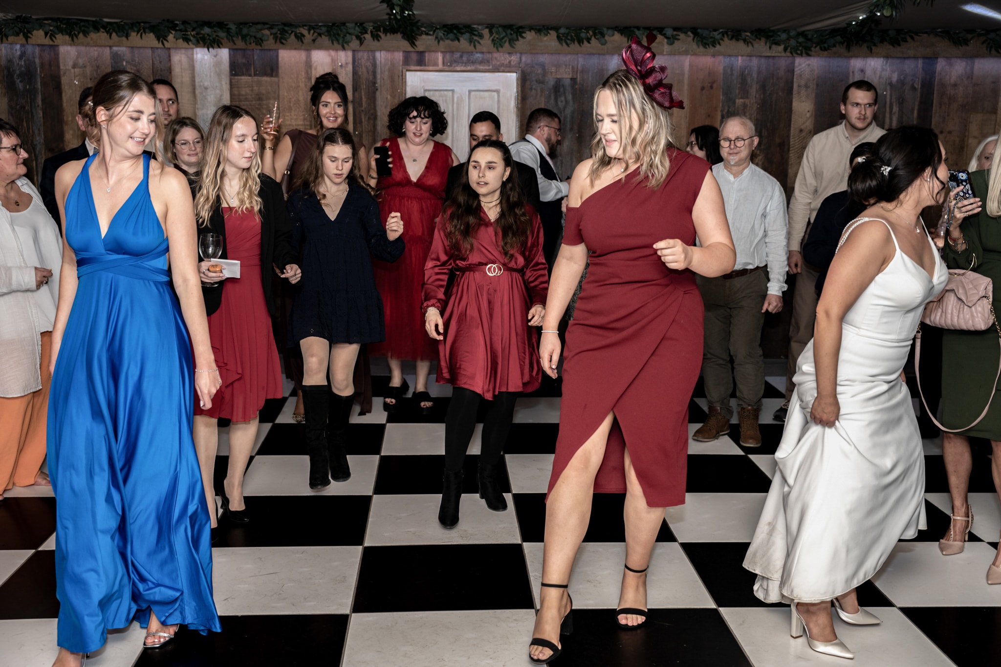 Wedding guests dancing on checkered floor at Notley Tythe Barn evening reception with bridesmaids in blue and red