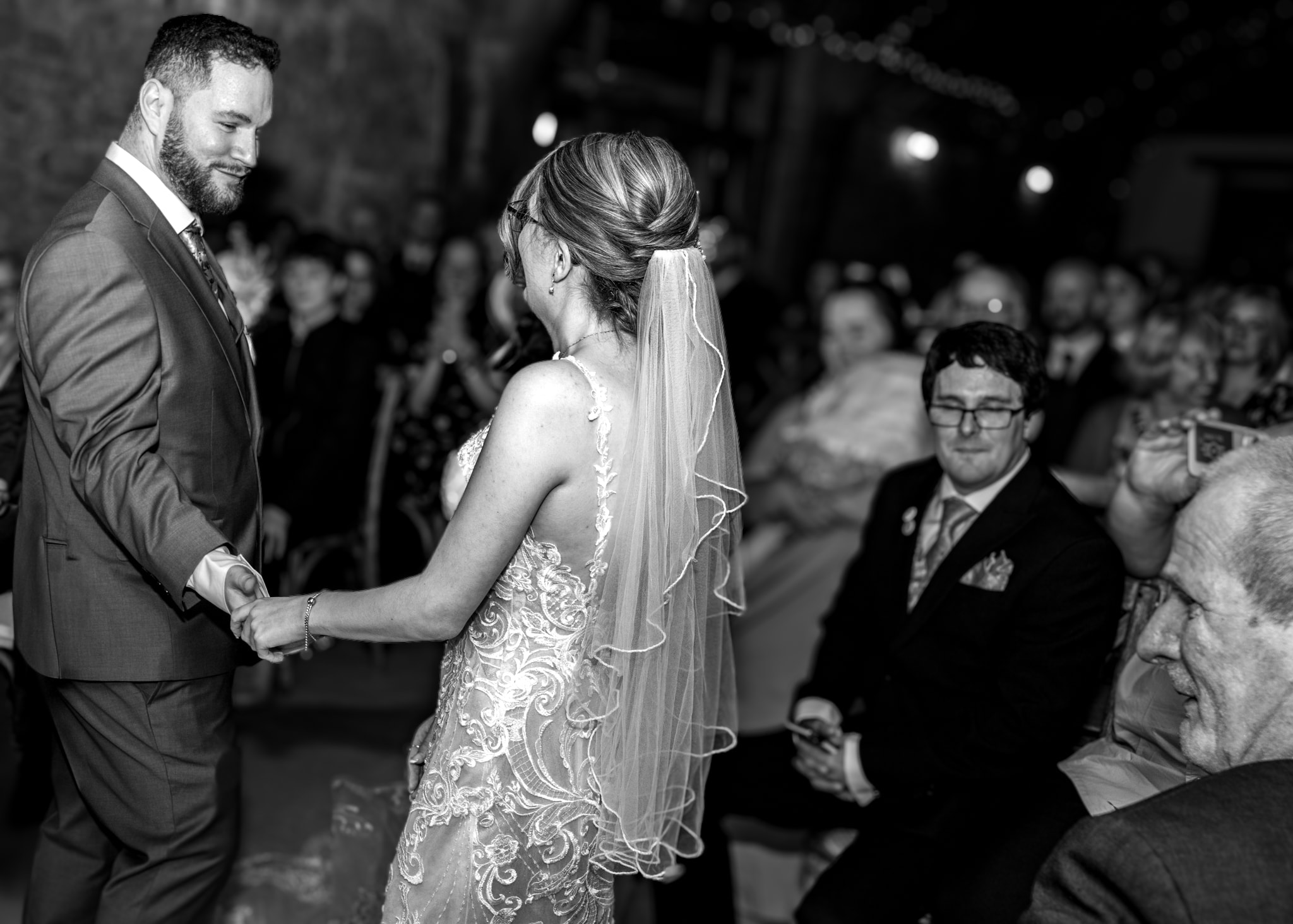 Bride and groom holding hands during wedding ceremony at Notley Tythe Barn in black and white with guests watching